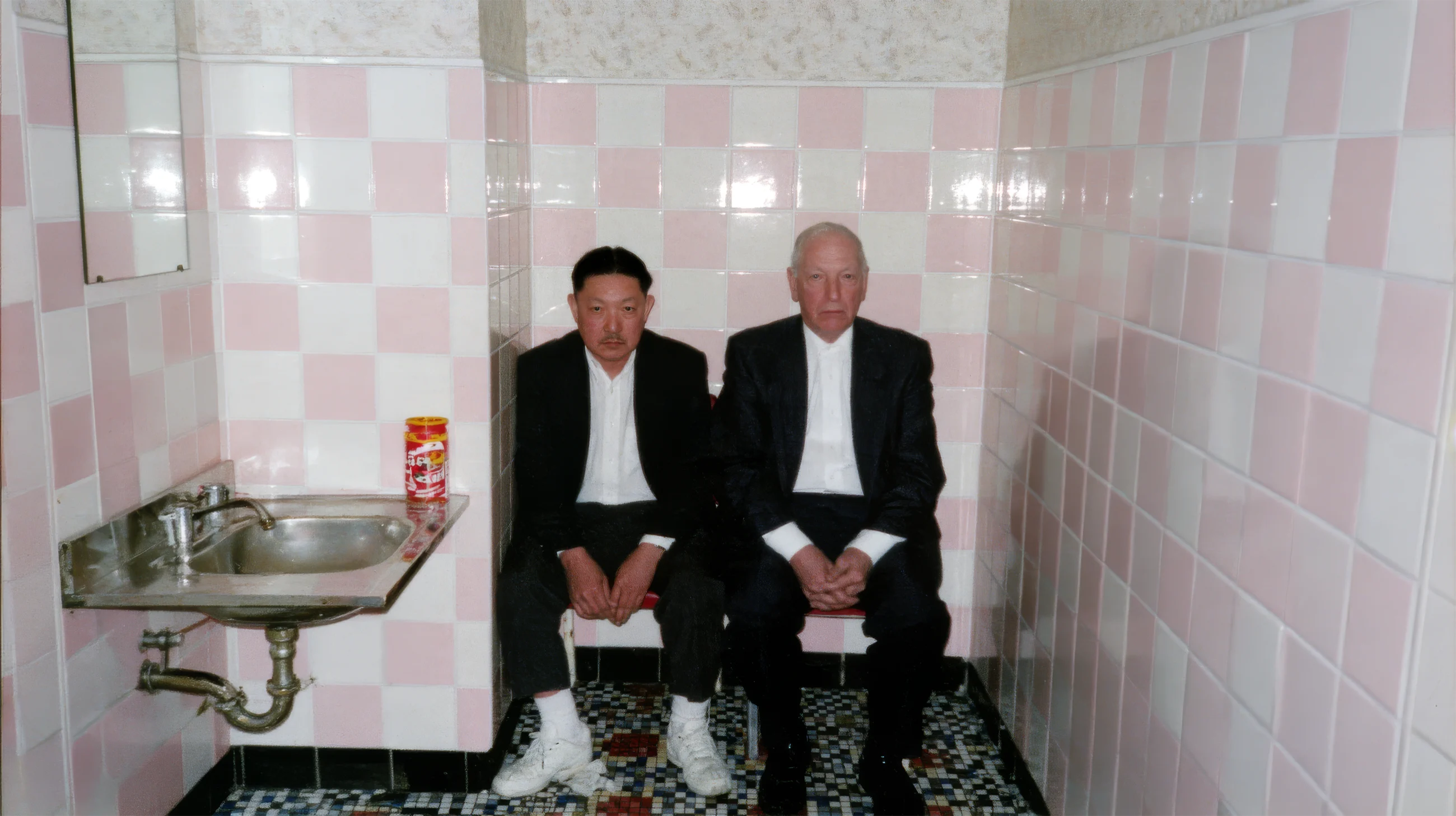 Everyday Absurdity, two men in dark suits sitting side by side in a pink-tiled room